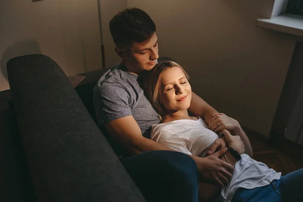 Menina loira encantadora deitada em seu amante caucasiano com olhos fechados enquanto sentados em um sofá juntos — Fotografia de Stock