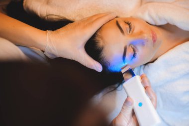 Dikkatli bir dermatolog esmer beyaz bir bayanla lazer seansı yapıyor.