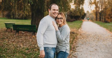 Parkta yürürken gülümseyen ve kocasını kucaklayan beyaz bir kadın.