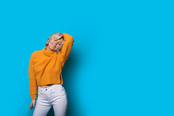 Розтяжка блондинка позує в жовтому светрі на синій стіні з вільним простором — стокове фото