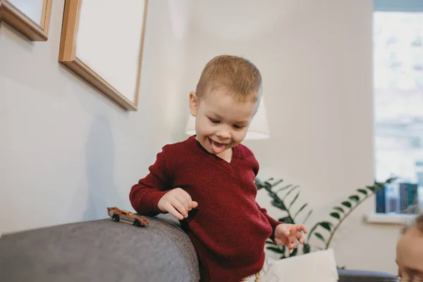 Niño caucásico infantil con el pelo rubio está jugando alegremente con su padre sentado en el sofá —  Fotos de Stock