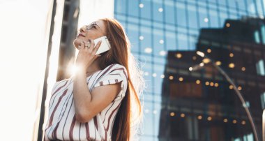 Kafkasyalı, kızıl saçlı, çilli iş kadını gözlüklerinden başka bir yere bakarken telefonla konuşuyor.