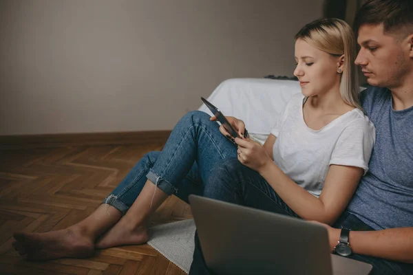 Fehér pár ül a padlón, laptopot és táblagépet használva, miközben keresnek valamit. — Stock Fotó