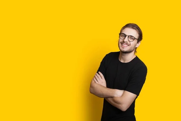 Homem caucasiano alegre com cabelos longos e barba está posando com as mãos cruzadas em uma parede amarela com espaço em branco — Fotografia de Stock