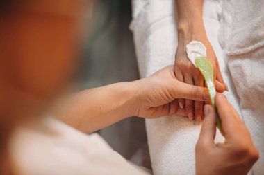 Genç spa çalışanı, müşteriyi bir sonraki ameliyata hazırlarken krem sürüyor.