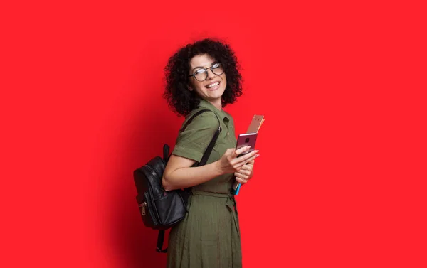 Studente caucasico è in posa su un muro rosso mentre digita qualcosa al telefono e in possesso di una borsa con alcuni libri — Foto Stock