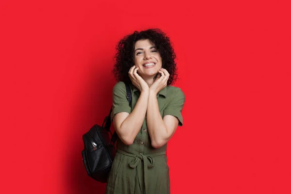 Delizia studente caucasico con i capelli ricci si sente felice mentre posa con una borsa su uno sfondo rosso — Foto Stock