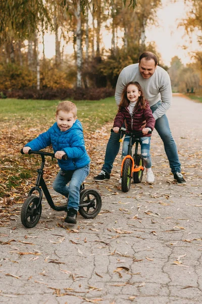 Beyaz bir baba çocuklarına sonbahar yürüyüşü sırasında bisiklet sürmeyi öğretiyor. — Stok fotoğraf