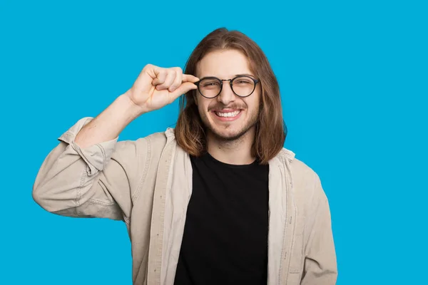 Caucasian man with long hair and beard looking through eyeglasses is smiling cheerfully on a blue wall — Stock Photo, Image