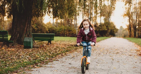 Genç beyaz kız parkta yürürken bisikleti dikkatle sürüyor. — Stok fotoğraf