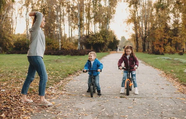 Güneşli bir sonbahar gününde bisiklete binen çocukları için beyaz bir anne başlangıç yapıyor. — Stok fotoğraf