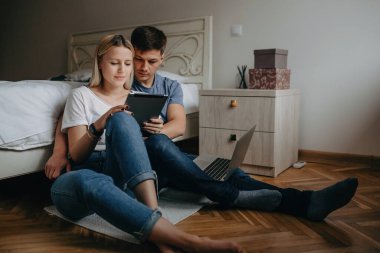 Beyaz bir çift yatak odasında yerde otururken tablete sarılıp göz gezdiriyorlar.