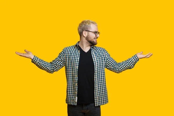 Homem caucasiano barbudo com cabelo loiro está comparando duas coisas de suas palmas enquanto posando em uma parede amarela — Fotografia de Stock