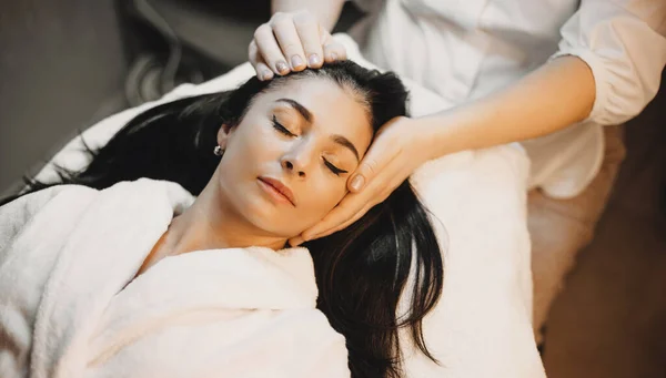 Brunett kaukasisk dam ljuger och har en huvud massage förfarande i en professionell spa salong — Stockfoto