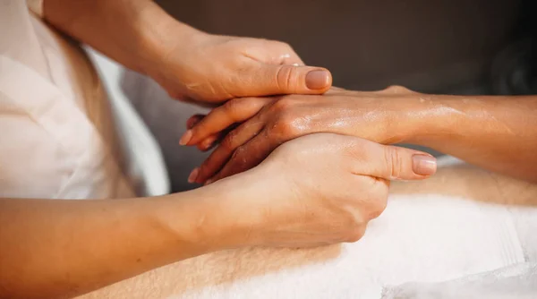 Jovem praticante caucasiano está massageando os clientes mão com uma loção natural durante um procedimento de spa — Fotografia de Stock