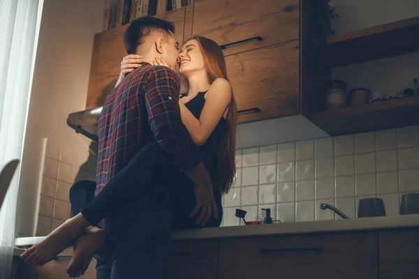 Η παθιασμένη κοκκινομάλλα με τις φακίδες αγκαλιάζει τον εραστή της ενώ τον φιλάει στην κουζίνα. — Φωτογραφία Αρχείου