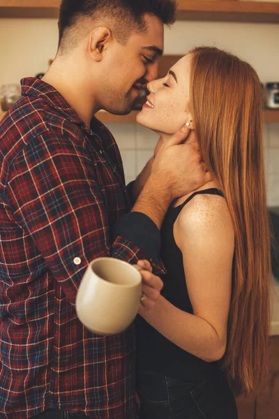 쾌활 한 백인 남녀가 커피 잔을 들고 부엌에서 서로 키스를 한다 — 스톡 사진