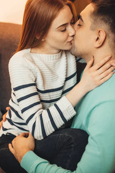 Härlig rödhårig flicka med fräknar omfamnar sin älskare och kysser medan omfamnas av honom på en soffa — Stockfoto