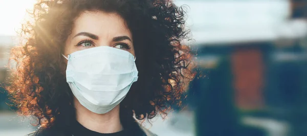 Güzel kıvırcık saçlı beyaz kadın özel maske takarken kendini virüslerden koruyor.