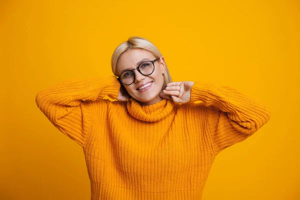 Dulce mujer caucásica con suéter agradable está tocando su cabello rubio mientras posa sobre un fondo amarillo — Foto de Stock