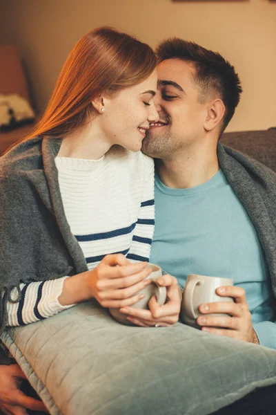 Adorável casal caucasiano ter uma pausa para o café enquanto sentado no sofá e beijando uns aos outros — Fotografia de Stock