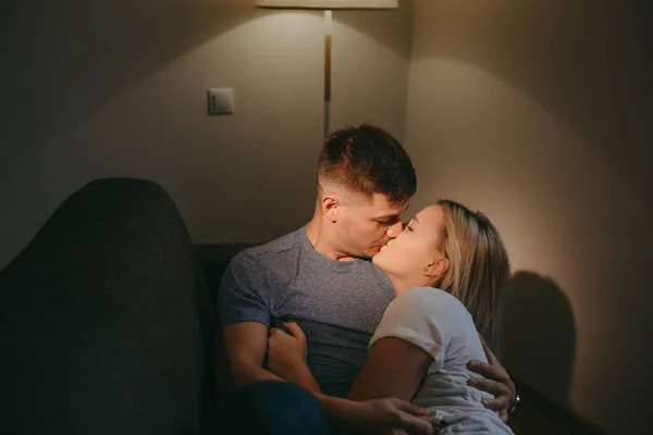 Kaukasiska par kysser när de ligger på en soffa under en söt kväll tillsammans — Stockfoto