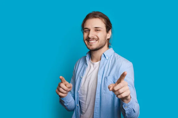 Hombre caucásico guapo con cerdas y pelo largo está apuntando a la cámara mientras sonríe sobre un fondo azul — Foto de Stock
