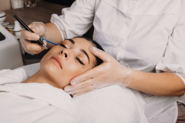 Güzel esmer, beyaz kadın, yüzü için spa ameliyatı olurken gözleri kapalı kanepede yatıyor.