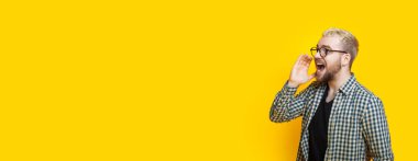 Sarışın, beyaz, sakallı ve gözlüklü bir adam sarı arka planda çığlık atıyor.