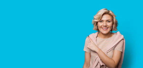 Beautiful blonde caucasian woman pointing to the blue free space near her — Stock Photo, Image