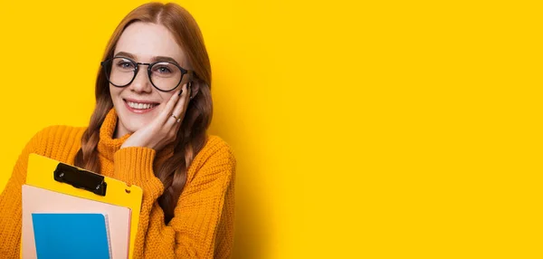 Close up portrait of a caucasian student with red hair and freckles holding some books and posing on a yellow wall with blank space — Stock Photo, Image