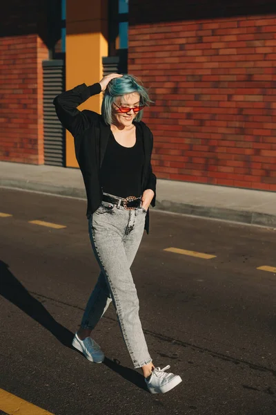 Blauw harige blanke vrouw met bril loopt op straat terwijl poseren tegen de zon — Stockfoto