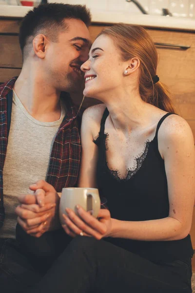 Caucasian man whispering something to his wife while having a coffee break in kitchen on the floor