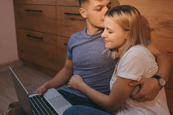 Homem caucasiano cuidadoso beijando sua esposa loira enquanto toma um chá juntos usando um laptop — Fotografia de Stock