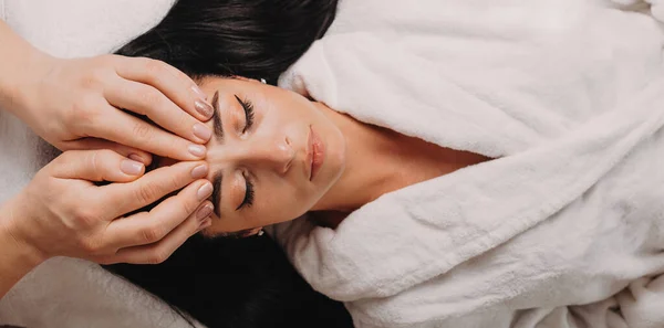 Jong masseur heeft een facial massage sessie met een brunette vrouw liggend op de bank — Stockfoto