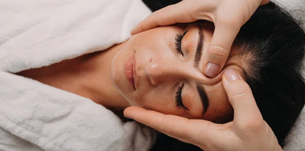 Портрет кавказької брюнетки лежить на дивані і масаж обличчя в салоні — стокове фото