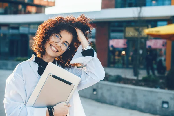 Encantadora mulher de negócios caucasiana tocando seu cabelo encaracolado enquanto posando com seu laptop fora — Fotografia de Stock