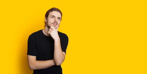 Homem caucasiano de cabelos longos com barba posando em um fundo amarelo com espaço em branco enquanto pensa em algo — Fotografia de Stock