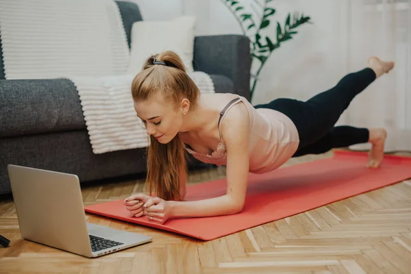 Donna con i capelli rossicci che praticano yoga sul pavimento mentre usano un computer — Foto Stock