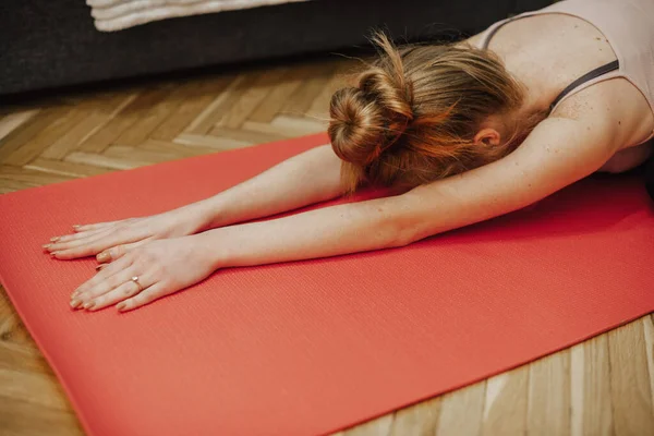 Jengibre mujer caucásica estirándose sobre una alfombra roja en el suelo mientras practica yoga — Foto de Stock