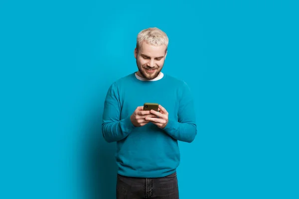 Homem caucasiano com cabelo loiro conversando com alguém enquanto posando em um fundo azul — Fotografia de Stock