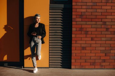 Mavi saçlı, güzel, şık bir bayan, elinde cep telefonu ve gözlük tutarken duvarda yatıyor.