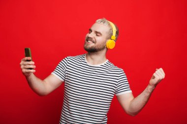 Kulaklıkla müzik dinlerken kırmızı arka planda dans eden sarı saçlı beyaz bir adam.