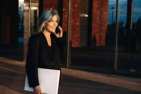 Imprenditore caucasico dai capelli blu che ha una discussione telefonica mentre cammina con un computer — Foto Stock