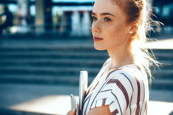 Wonderful ginger lady with freckles is looking away thinking about something while posing with some modern gadgets — Stock Photo, Image