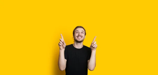 Sonriente hombre caucásico con barba y pelo largo señala hacia el espacio libre amarillo por encima de él — Foto de Stock