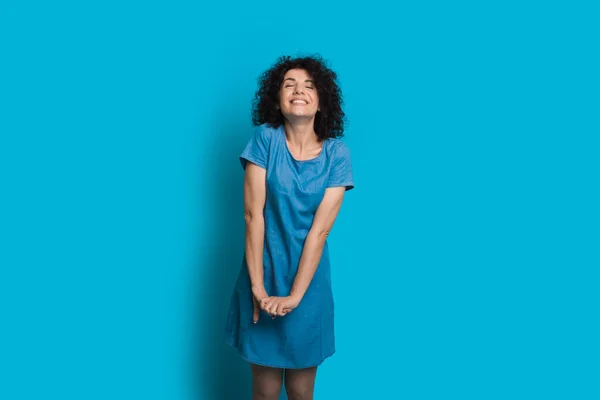 Dolce donna caucasica con i capelli ricci è in posa con gli occhi chiusi su una parete blu con spazio libero — Foto Stock