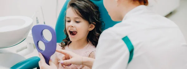 Klein blank meisje kijkend in de spiegel na een tandheelkundige operatie aan de stomatologie — Stockfoto