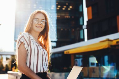 Güzel, kızıl saçlı, çilli bayan dışarıda otururken dizüstü bilgisayar kullanıyor.