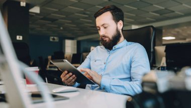 İş yerinde çalışırken tablet kullanan sakallı beyaz bir genç.